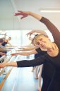 Smiling adult woman stretching and doing gymnastics in ballet class